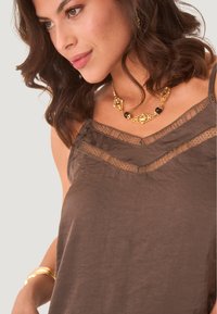 Top de tirantes marrón con delicado encaje en el escote, que presenta tirantes finos. Collar dorado con acentos en negro y dorado.
