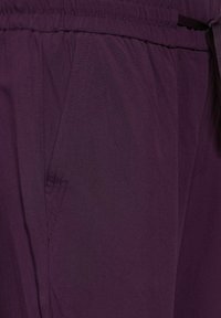 Lila byxor i lätt tyg med elastisk midja, med sidfickor och kontrasterande sömmar.