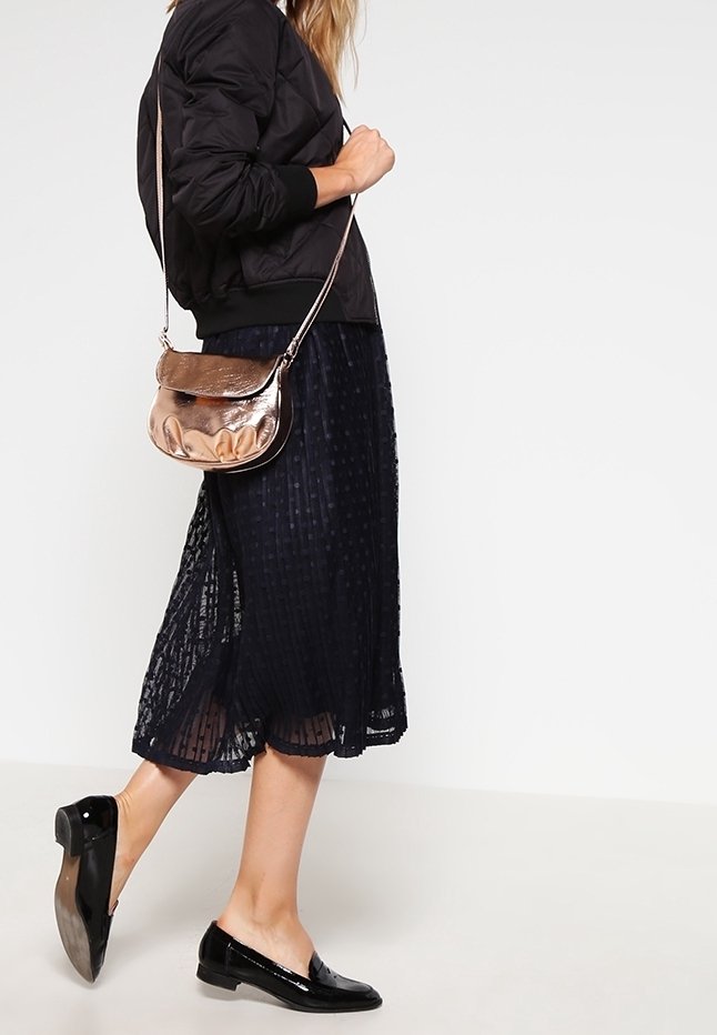 Giubbotto bomber nero con polsini a coste, gonna plissettata blu navy, ballerine nere lucide e borsa a tracolla metallizzata rosa oro.