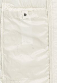 Intérieur d'une doudoune blanche avec une texture lisse semblable à du satin, comportant un bouton-pression et une étiquette d'entretien avec un texte circulaire.