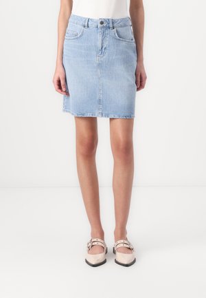 Lyseblåt denimskørt båret med hvid top og beige spidse flade sko med ankremme, vist fra talje til fødder på hvid baggrund.
