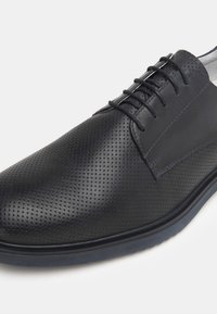 Scarpe da uomo in pelle nera con texture perforata, design con lacci e suola in gomma a contrasto. Presentano pannelli lisci e strutturati.