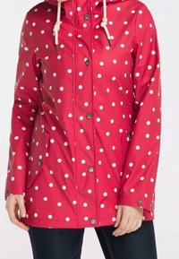 Červená voděodolná bunda s bílými puntíky, se zipovými kapsami a kapucí na stažení. Knoflíky na přední straně dodávají funkční detail.