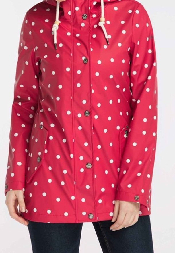 Červená voděodolná bunda s bílými puntíky, se zipovými kapsami a kapucí na stažení. Knoflíky na přední straně dodávají funkční detail.