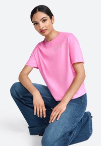 Tricou din bumbac roz cu guler rotund și mâneci scurte, având brodat pe față "Cocktail Club" cu fir deschis.