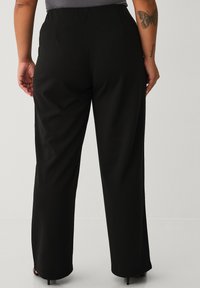 Pantalones negros de pierna ancha con una textura suave, que cuentan con dos bolsillos traseros y una cintura de tiro medio, complementados con una camiseta gris ajustada.