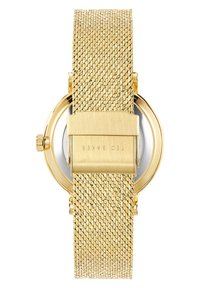 Zlaté hodinky s kulatým pouzdrem, hladkým pozlaceným kováním a vyraženým názvem značky. Mají texturovaný pásek, který zlepšuje úchop a styl.