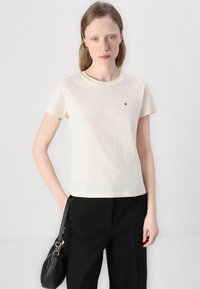 T-shirt a maniche corte color crema in cotone morbido, con un piccolo logo sul petto. Indossato con pantaloni neri su misura e una borsa.