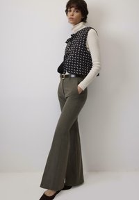 Crtni prsluk s crno-bijelim uzorkom preko krema visokog ovratnika, uparen s maslinasto zelenim flared hlačama i smešnim cipelama na petu.
