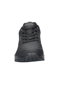 Zwarte sportieve schoen met gestructureerde synthetische bovenkant, vetersluiting en rubberen buitenzool met profielen voor grip. Merknnaam gekerfd op de tong.