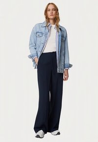 Giacca di denim azzurro chiaro sopra una T-shirt bianca, abbinata a pantaloni larghi blu navy e scarpe sportive grigie. Design semplice, stile casual.