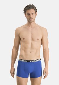 Boxers bleus en tissu extensible avec une ceinture noire portant le nom de la marque "HEAD" en lettres blanches.