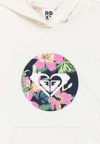 Sudadera de color crema claro con un gráfico circular que presenta un patrón floral en rosa y verde, centrado alrededor de un logotipo de corazón blanco.