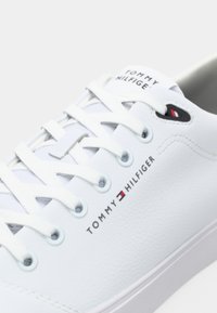 Vita lädersneaker med vita snören, som har Tommy Hilfiger-logotyp och flagga på sidan och tungan.