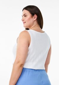 Top sin mangas blanco con un escote en forma de U y un patrón texturizado, combinado con pantalones azul claro. Muestra la vista trasera y los detalles de los hombros.