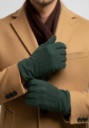 Mann trägt dunkelgrüne Handschuhe über einem camel-farbenen Mantel mit einem braunen Schal und richtet einen Handschuh mit der anderen Hand.