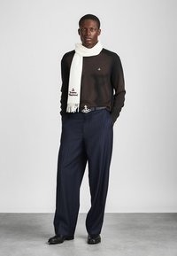 Juodas megztinis iš mezginio, balta šalikė, mėlyni kelnės su baltomis juostelėmis, juodas diržas su sidabrinėmis detalėmis ir juodi batai. Švarus, modernus siluetas.