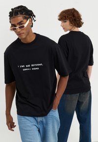 Black cotton t-shirt with short sleeves and a relaxed fit, featuring white text that reads "I LIKE BAD DECISIONS, SORRY MAMA."