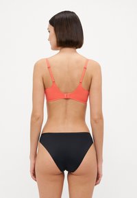 Koraal kleurige beha met verstelbare banden, haaksluiting aan de achterkant; gecombineerd met zwarte high-waisted bikini onderkant, gladde stof, minimalistisch ontwerp.