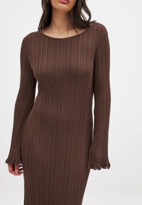 Robe longue à manches longues marron à col bateau et avec des manches évasées, fabriquée en tissu extensible, présentant une texture subtile et un design ajusté.