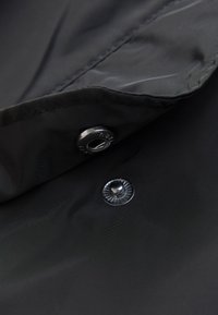 Tissu noir à texture lisse, avec un bouton-pression en métal et des détails de couture le long du bord.