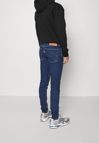 Jeans blu slim-fit in denim testurizzato, con una patch in pelle firmata, tasche posteriori e abbinati a scarpe sportive argento.