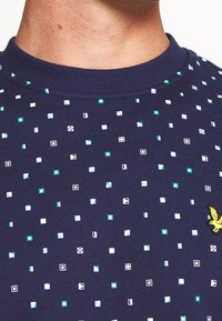 Maglione blu navy con punti testurizzati bianchi, verdi e azzurri. Presenta un colletto a girocollo a coste e un logo di un'aquila ricamato.