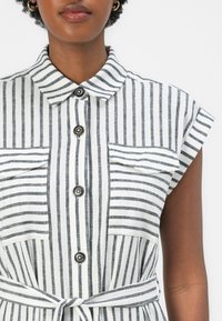 Rochie cu dungi, având mâneci scurte, închidere cu nasturi și două buzunare frontale; fabricată dintr-un material ușor, în dungi albe și gri închis.