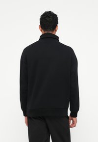 Zwarte sweatshirt met een omgeslagen kraag, lange mouwen en een ontspannen pasvorm. Heeft geribde manchetten en een zoom. Materiaal lijkt zacht en textuur te hebben.