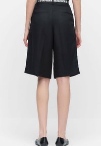 Mustat räätälöidyt shortsit rentoa istuvuutta, joissa on sileä pinta, reiden puoliväliin ulottuva pituus ja kaksi takataskua, suunniteltu rakenteelliseen eleganssiin.