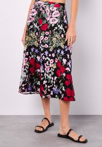 Schwarzer Midirock mit buntem besticktem Blumenmuster in Rot, Pink, Weiß und Lila; hat eine fließende Form und einen breiten Bund.