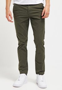 Olivgrön bomullschinos med slim fit, med sidfickor och bälteshällor, i kombination med vita sneakers. Slät textur.