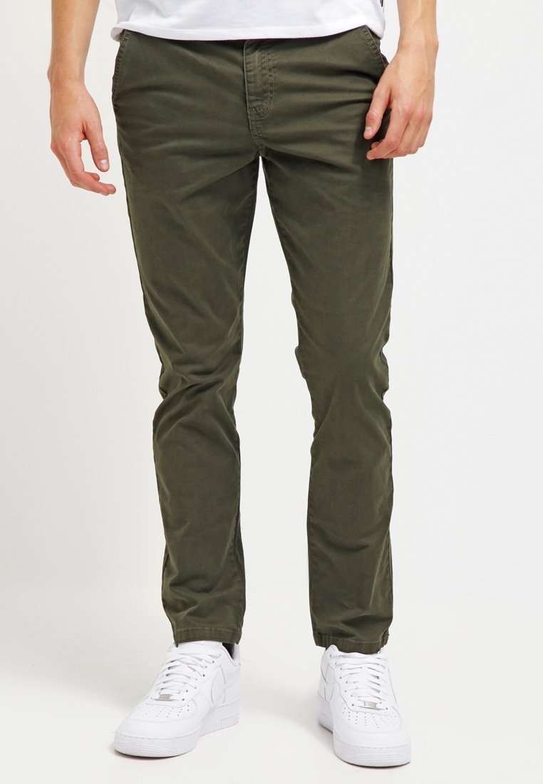 Olivgrön bomullschinos med slim fit, med sidfickor och bälteshällor, i kombination med vita sneakers. Slät textur.