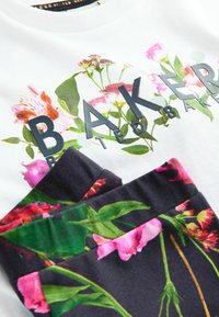 Valge sweatshirt, millel on lilleline trükk ja tume kiri "BAKER". Alumine osa on tume kangas, millel on mitmevärviline lillemuster.