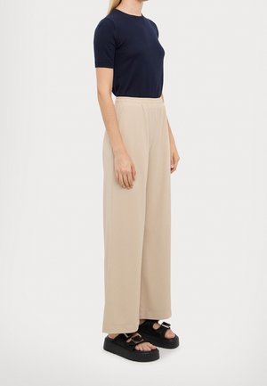 Haut à manches courtes marine associé à un pantalon large beige clair ; sandales à plateforme noires avec des brides texturées. Coupe lisse et décontractée.