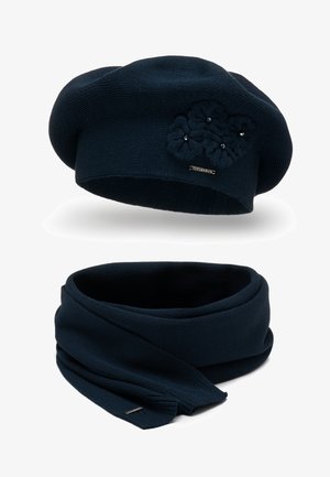 Béret tricoté marine avec des détails floraux et un logo métallique. Écharpe infinity assortie, tous deux fabriqués à partir d'un tissu texturé doux.