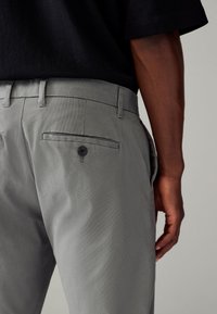 Pantalons texturés gris avec une finition lisse, dotés d'une poche arrière à bouton et de passants de ceinture, associés à une chemise noire.