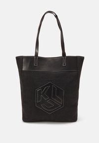 Bolso tote negro con un cuerpo de tela texturizada y acentos de cuero sintético suave. Incluye un logo hexagonal negro con costuras blancas.