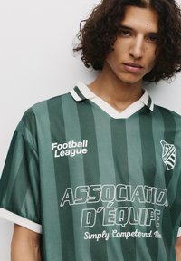 Grønstribet fodboldtrøje med en hvid krave. Har "Football League"-logoet og teksten "ASSOCIATION D'ÉQUIPE" i kontrasterende hvid.