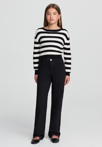 Czarny i biały sweter w paski z okrągłym dekoltem, w zestawieniu z czarnymi spodniami o wysokim stanie i szerokimi nogawkami oraz płaskimi czarnymi butami.