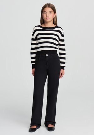 Pullover a righe bianche e nere in maglia con scollatura rotonda, abbinato a pantaloni neri a vita alta e larga con scarpe nere basse.