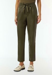 Pantalon en simili cuir vert olive avec une taille élastique, cordon de serrage réglable et une coupe fuselée. Texture lisse avec des coutures minimales.