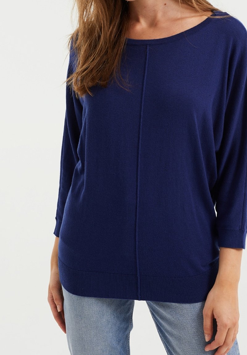 Námořnický modrý svetr s uvolněným střihem, širokým výstřihem a žebrovanými manžetami a lemem. Měkká textura s centrálním švem.