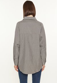 Camicia a maniche lunghe grigia con sottili righe verticali, dotata di colletto e orlo curvo. Realizzata in un tessuto morbido e strutturato.