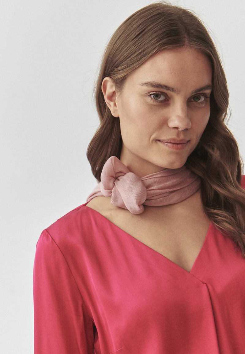 Blouse rose vif avec un décolleté en V profond et des manches longues, associée à une écharpe rose clair douce, nouée autour du cou.