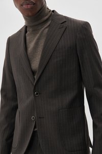 Donkerbruine pinstripe pak met enkele knoop sluiting, notch revers en klepzakken. Gelaagd over een geribde bruine turtleneck.