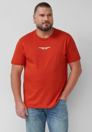 T-shirt in cotone rosso con scollatura rotonda e maniche corte, caratterizzato da dettagli testuali bianchi sul davanti. Abbinato a jeans di denim.