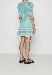 Vestido verde con estampado, mangas abullonadas, dobladillo en capas y acentos a rayas. Combinado con sandalias negras con tiras. Textura de tela suave.