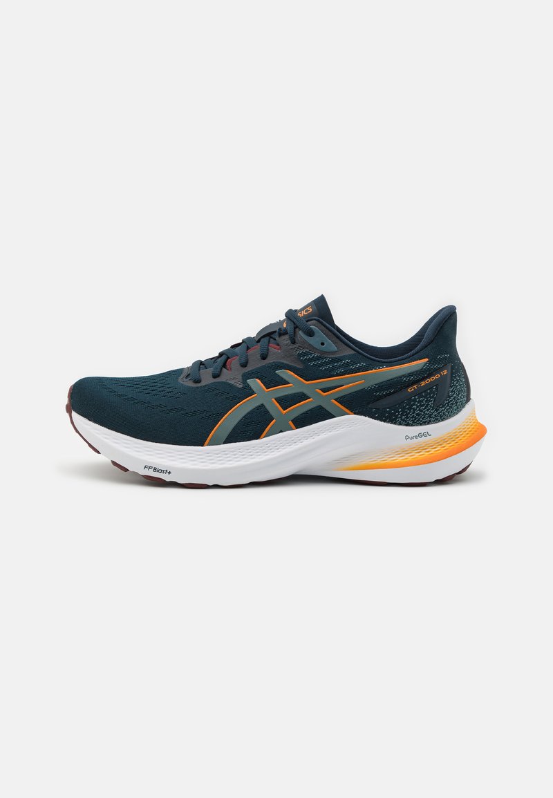 Zapatilla deportiva masculina en malla verde oscuro con acentos en naranja y amarillo. Presenta una suela blanca acolchada, parte superior texturizada y cordones planos.