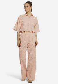 Pink, eyelet-patterned two-piece outfit with cropped blouse featuring scalloped edges and loose-fitting, wide-leg pants with an elastic waistband.
